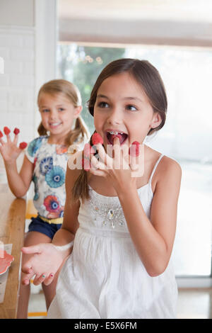 Zwei Schwestern mit Himbeeren an ihren Fingern in Küche Stockfoto