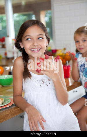 Zwei schelmische Schwestern mit Himbeeren an ihren Fingern in Küche Stockfoto