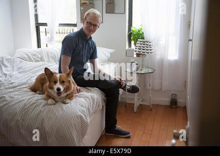 Niedliche Corgi Hund auf Bett liegend beobachtet von junger Mann Stockfoto