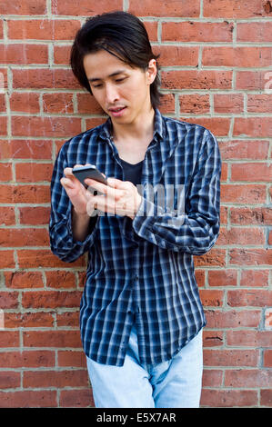 Mitte erwachsener Mann gelehnt Wand SMS auf smartphone Stockfoto