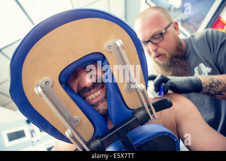 Männliche Kundschaft Gesicht zwischen Kopfstütze im Tattoo-Studio Stockfoto