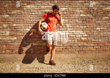 Junge männliche Fußballspieler im Chat auf Smartphone auf einer Brache Stockfoto