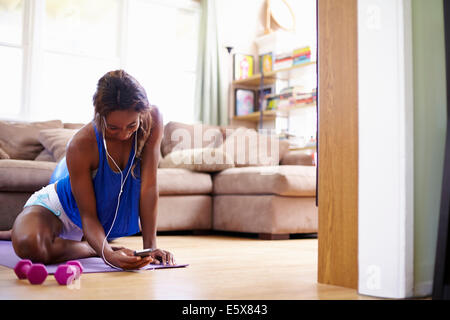 Junge Frau Ausübung Erdgeschoss Wohnzimmer während Smartphone betrachten Stockfoto