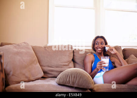 Junge Frau auf eine Trainings-Pause im Chat auf Smartphone im Wohnzimmer Stockfoto