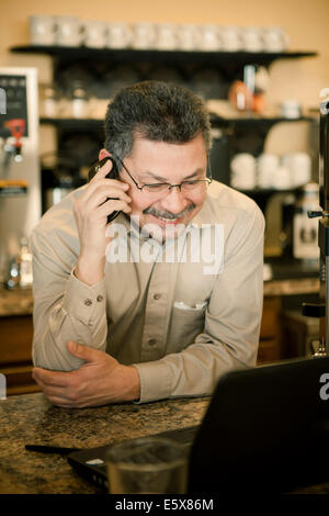 Ältere männliche Café-Besitzer im Chat auf Smartphone am Café-Schalter Stockfoto