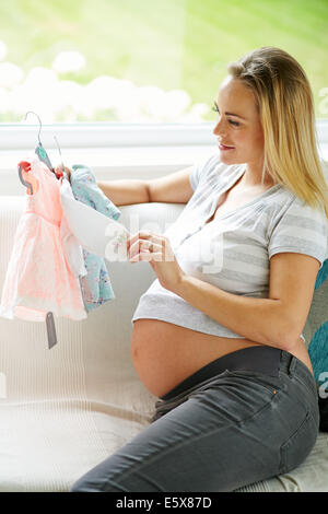 Schwangere Frau betrachten Baby-Kleidung Stockfoto
