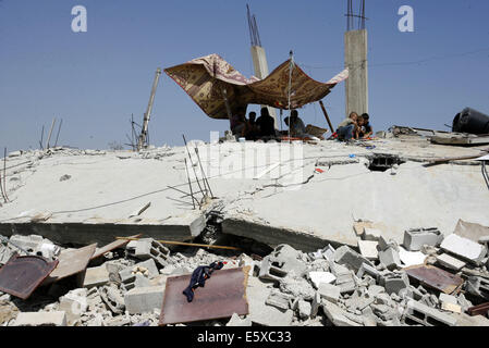 Khan Younis, Gazastreifen, Palästinensische Gebiete. 7. August 2014. Palästinenser sitzen auf den Trümmern ihres zerstörten Hauses, das bei einem israelischen Luftangriff auf Abasan, östlich der südlichen Gazastreifen Stadt von Khan Yunis und nahe der Grenze zu Israel am 7. August 2014 getroffen wurde. Mehrere Menschen starben bei dem Angriff Credit: Abed Rahim Khatib/APA Bilder/ZUMA Draht/Alamy Live News Stockfoto