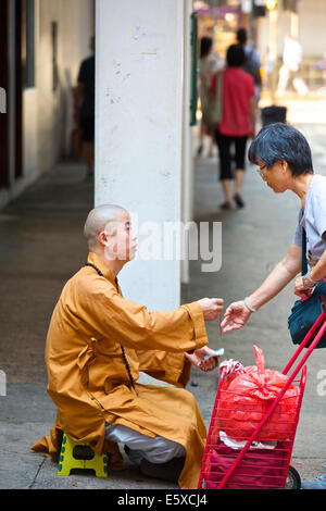 Chinesische Frau und ein junger buddhistischer Mönch auf Chun Yeung Street, Hong Kong. Stockfoto