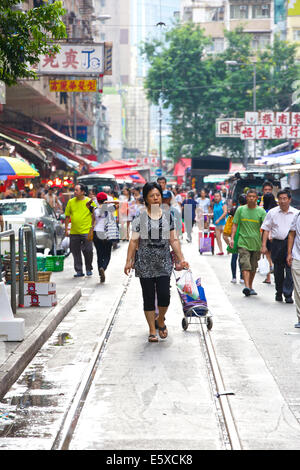 Sonntag Einkaufen. Chinesische Frau Spaziergänge entlang der Straßenbahnschienen auf Chun Yeung Street, Hong Kong. Stockfoto