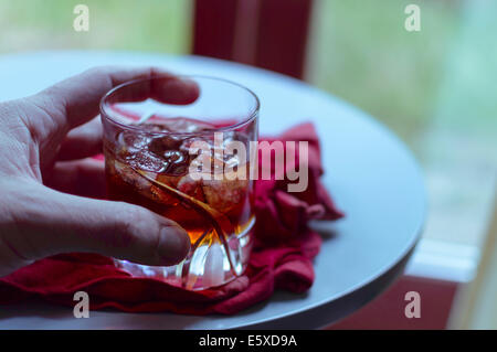 Ein Glas Amaretto mit Eis, das von einer Hand gehalten wird Stockfoto