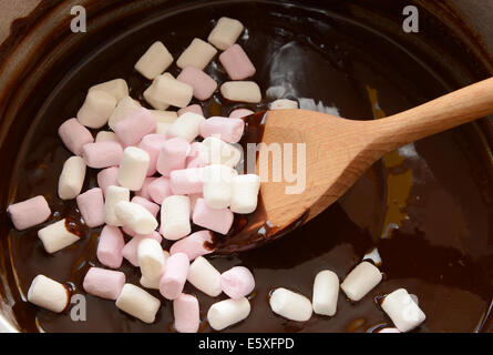 Rühren, rosa und weißen Mini Marshmallows in geschmolzene Schokolade mit einem Holzlöffel, steinigen Weg zu machen Stockfoto