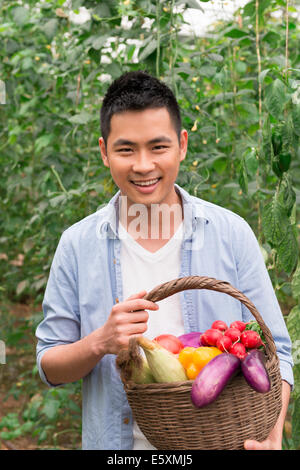 Junger Bauer hält einen Korb mit frischem Gemüse, Ernte genießen. Stockfoto