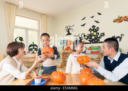 Lehrer und Schüler schnitzen Kürbisse im Klassenzimmer, lächelnd. Stockfoto