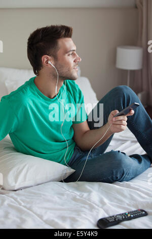 Junger Mann sitzt auf Bett Musikhören mit smartphone Stockfoto