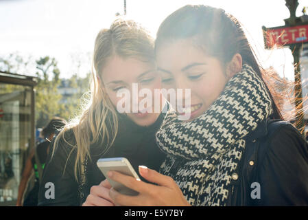 Junge Frauen, die im freien Blick auf Handy zusammen Stockfoto