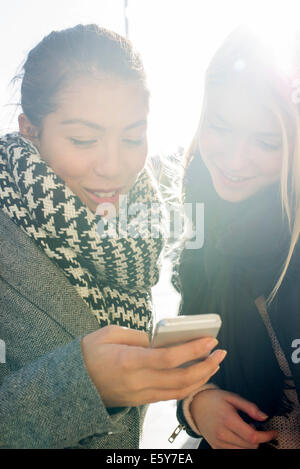 Junge Frauen, die im freien Blick auf Handy zusammen Stockfoto