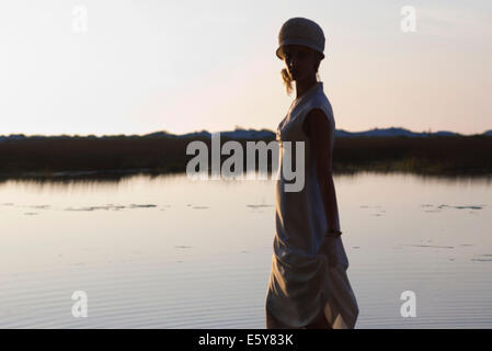 Junge Frau trägt Kleid vor See in der Abenddämmerung Stockfoto