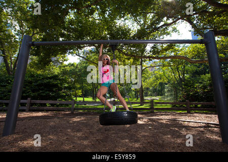 Young blonde sportliche Frau sitzen und Schaukeln auf einer Reifenschaukel im Central Park Stockfoto