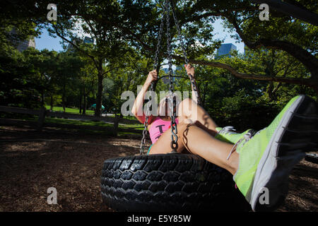 Young blonde sportliche Frau sitzen und Schaukeln auf einer Reifenschaukel im Central Park Stockfoto