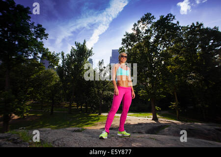 Young blonde sportliche Frau hält einen roten Regenschirm im Central Park Stockfoto