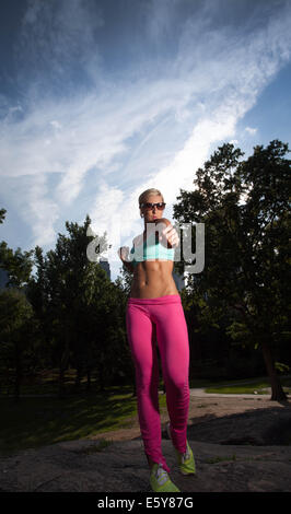 Young blonde sportliche Frau hält einen roten Regenschirm im Central Park Stockfoto