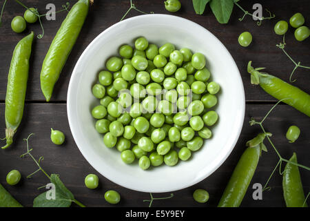 Grüne Erbsen in Schüssel auf Holztisch Hintergrund. Ansicht von oben Stockfoto