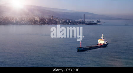 Ein Frachtschiff schwimmt auf Wasser mit Blick auf eine Bucht bei Sonnenaufgang, im Libanon. Stockfoto