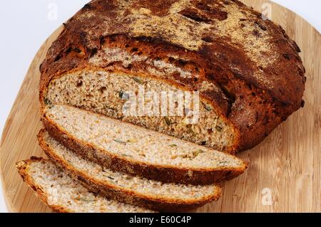 Hausgemachte frische ausgesät Brotlaib, teilweise aufgeschnitten, auf einem Holzbrett vor einem einfarbigen Hintergrund. Stockfoto