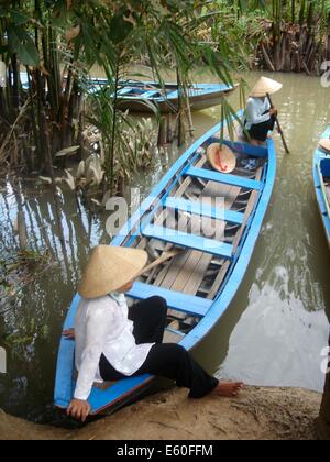 Eine vietnamesische Frau trägt einen traditionellen konischen Hut, sitzt auf ihrem Holzboot im Mekong-Delta, in der Nähe von Ho-Chi-Minh-Stadt, Vietnam Stockfoto