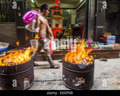 Bangkok, Thailand. 10. August 2014. Ein Mann geht durch Fässer brennen Joss Papier und Hölle Geld vor einem Haus in einer Seitenstraße im Abschnitt Chinatown von Bangkok. Der siebte Monat des chinesischen Mondkalenders nennt man '' Ghost Monat '' während die Geister und Gespenster, einschließlich derjenigen der verstorbenen Vorfahren aus dem unteren Bereich kommen. Es ist üblich, dass Chinesen um Verdienst im Laufe des Monats durch Brennen '' Hölle Geld '' und die Geister zu essen präsentieren. Bildnachweis: Jack Kurtz/ZUMA Draht/Alamy Live-Nachrichten Stockfoto