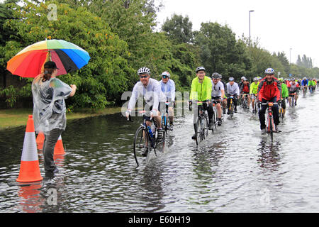 Sonntag, 10. August 2014. East Molesey, Surrey, UK. Radfahrer durchpflügen eine überflutete Straße nach Starkregen durch Reste der Hurrikan Bertha Hits aufsichtsrechtlichen RideLondon-Surrey 100 verursacht. 24.000 Amateur-Radfahrer nahmen Teil an der Veranstaltung der 100miles abdeckt und meistens folgt die Route in London 2012 Olympischen Straßenrennen verwendet. Die Strecke wurde jedoch aufgrund des schlechten Wetters, 86miles verkürzt. Bildnachweis: Ian Flasche/Alamy Live-Nachrichten Stockfoto