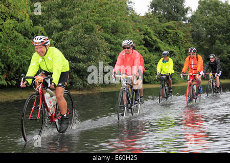 Sonntag, 10. August 2014. East Molesey, Surrey, UK. Radfahrer durchpflügen eine überflutete Straße nach Starkregen durch Reste der Hurrikan Bertha Hits aufsichtsrechtlichen RideLondon-Surrey 100 verursacht. 24.000 Amateur-Radfahrer nahmen Teil an der Veranstaltung der 100miles abdeckt und meistens folgt die Route in London 2012 Olympischen Straßenrennen verwendet. Die Strecke wurde jedoch aufgrund des schlechten Wetters, 86miles verkürzt. Bildnachweis: Ian Flasche/Alamy Live-Nachrichten Stockfoto