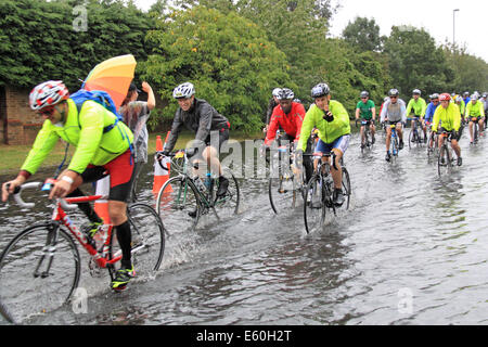 Sonntag, 10. August 2014. East Molesey, Surrey, UK. Radfahrer durchpflügen eine überflutete Straße nach Starkregen durch Reste der Hurrikan Bertha Hits aufsichtsrechtlichen RideLondon-Surrey 100 verursacht. 24.000 Amateur-Radfahrer nahmen Teil an der Veranstaltung der 100miles abdeckt und meistens folgt die Route in London 2012 Olympischen Straßenrennen verwendet. Die Strecke wurde jedoch aufgrund des schlechten Wetters, 86miles verkürzt. Bildnachweis: Ian Flasche/Alamy Live-Nachrichten Stockfoto