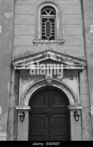 Byzantinische Kirche außen mit Alpha und Omega eingravierte Inschrift. Gewölbten Holztor und verwitterte Wand schwarz und weiß. Stockfoto