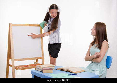 Schüler an der Tafel steht, der Lehrer sitzt an seinem Schreibtisch und hört auf den Schüler Stockfoto