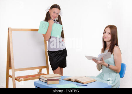 Schüler an der Tafel steht, der Lehrer sitzt an seinem Schreibtisch und hört auf den Schüler Stockfoto