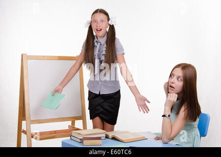 Schüler an der Tafel steht, der Lehrer sitzt an seinem Schreibtisch und hört auf den Schüler Stockfoto