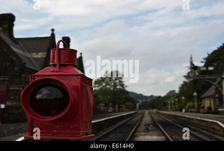 Bahn Wache rot lackierten Öllampe Licht ausgestattet auf Bahnübergang Barriere Darley Dale entfernten Bahnhof im Hintergrund Stockfoto