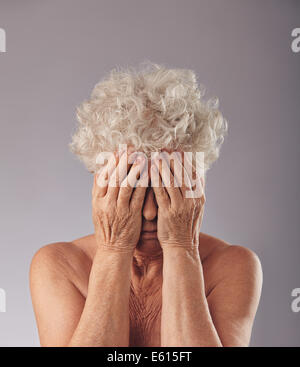 Porträt einer Frau mit dem Kopf in die Hände vor grauem Hintergrund verärgert. Traurige senior Frau bedeckte ihr Gesicht. Stockfoto