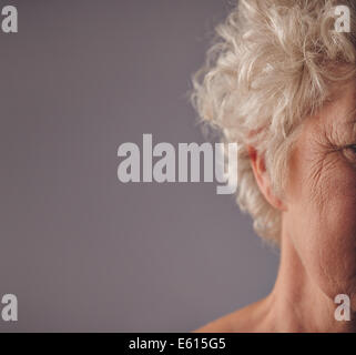 Ältere Frau Gesicht mit faltige Haut auf grauem Hintergrund abgeschnitten. Krähenfüße auf Augen der alten Frau. Stockfoto