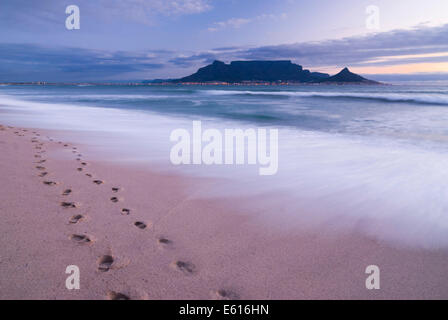 Table Mountain, Löwenkopf und Teufels Peak im Abendlicht, Panoramablick über Kapstadt, Fußabdrücke am Bloubergstrand Stockfoto