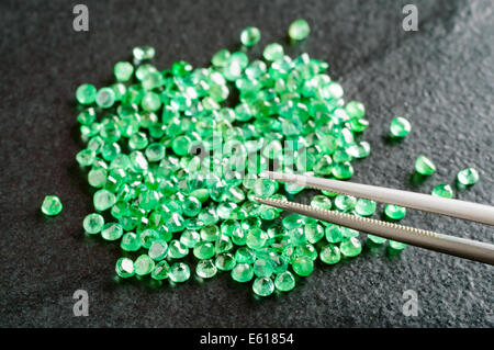 Haufen von Grün, Runde Smaragde auf schwarzen Steinplatte geschnitten. Ein Smaragd von Pinzette gehalten. Stockfoto