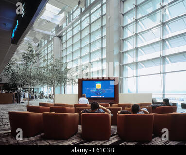 Reisende, die entspannen und Fernsehen vor Abflug am terminal 3 des Singapore Changi Airport. Stockfoto