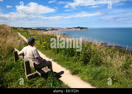 Mann sitzt auf einer Bank an der Cleveland Weise mit Blick auf South Bay Scarborough North Yorkshire England Stockfoto