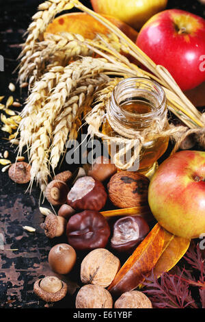 Glasglas Honig mit Äpfel, Ohren von Weizen, Kastanien und Walnüsse über schwarzer Holztisch Stockfoto