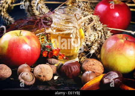 Glasglas Honig mit Äpfel, Ohren von Weizen, Kastanien und Walnüsse über schwarzer Holztisch Stockfoto