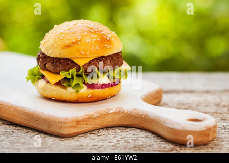 Lecker Burger mit Käse, Salat, Zwiebeln und Tomaten serviert auf einem Holztisch im freien Stockfoto