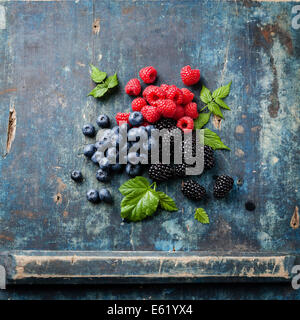 Mischung aus frischen Beeren mit Blättern auf blauem Hintergrund aus Holz Stockfoto