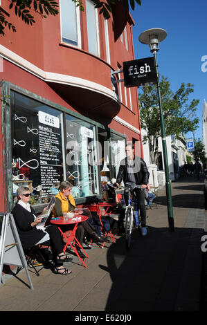 Menschen und Fahrräder vorbei an Cafés, Seite Fuß Restaurants und Pubs im Zentrum von Reykjavik an einem sonnigen Tag in Island Stockfoto