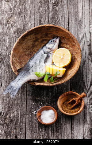 Seebarsch frischen rohen Fisch mit Salz, Gewürzen und Zitrone auf strukturierten hölzernen Hintergrund Stockfoto